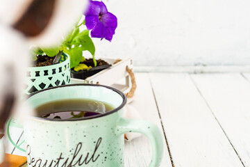 Close-up of a cup of tea on a wooden white table with blurred background, front blur. Still life with flower, book, teaspoon, cotton box. Spring breakfast. Copy space.