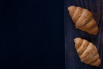 Fresh croissants close up on a wooden stand with cinnamon. On a dark background.
