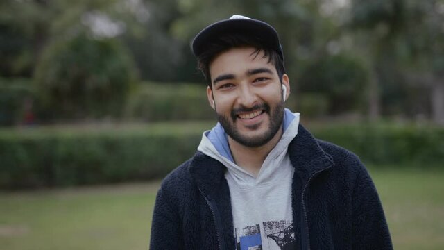 shot of a cheerful young Indian handsome man with broad smile on the face standing in a public park looking at camera 