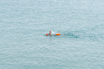 long-distance swimmer with orange cap and dry bag swimming in endless open ocean water