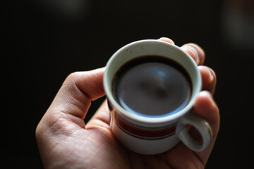 .hand picks up porcelain coffee cup with dark background