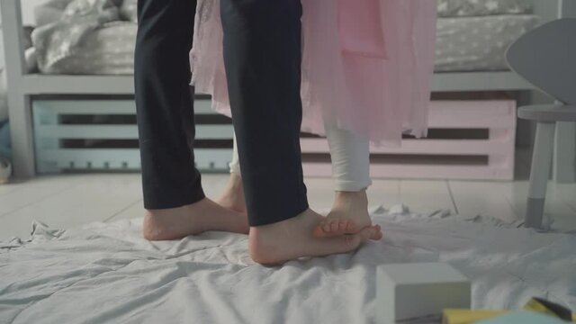 Father's day. Little daughter dances on her daddy's feet at home.