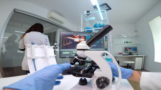 FPV of medical scientist looking under microscope, analyzes petri dish sample in equipped lab. Medical stuff examining vaccine development using high tech researching treatment against covid19 virus