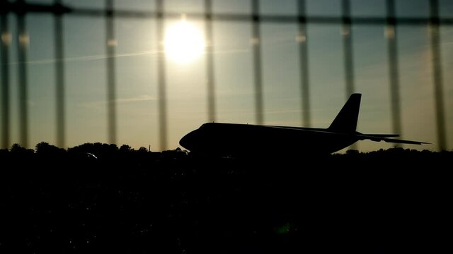 Dark silhouette of an airplane at sunset approach in the airport a beautiful sky, aircraft. In foreground is barrier grid