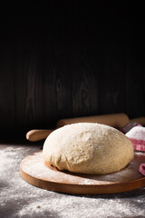Homemade wholemeal rye wheat dough for bread on wooden table with flour, rolling-pin, dark rustic background.