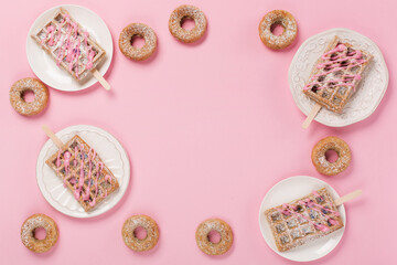 Traditional belgian waffles with sprinkles and delicious doughnuts with powdered sugar on pastel pink table. Top view, flat lay, copy space. Food background for party, birthday, valentines day.