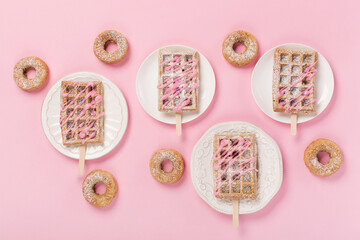 Fototapeta na wymiar Traditional belgian waffles with sprinkles and delicious doughnuts with powdered sugar on pastel pink background.