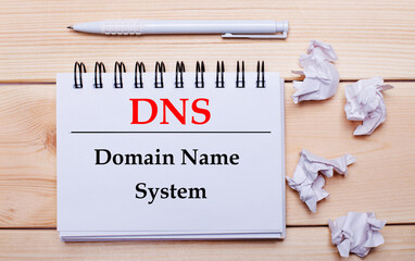 On a wooden background, a white notebook with the inscription DNS Domain Name System, a white pen...