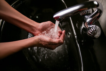 Washing the hands of a teenager in the sink under the tap with clean water. black sink, modern bathroom interior style.