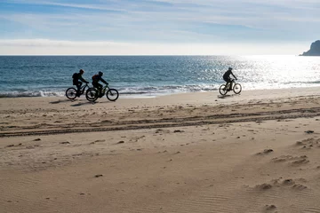 Cercles muraux Plage de Bolonia, Tarifa, Espagne silhouette of three bikers cruising along a secluded beach with fat tire bikes