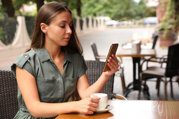 Young woman unlocking smartphone with facial scanner in outdoor cafe. Biometric verification