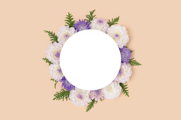 Wreath made of dahlia and green leaves on a beige background. Flower round frame with copyspace.