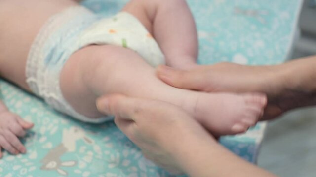 Mom massages her baby's feet close up. Mother's hands mass little child's legs. Childcare and motherhood concept.
