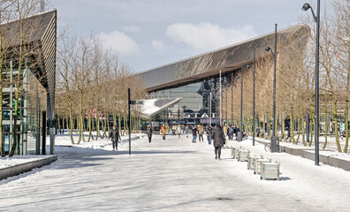 Fototapeta na wymiar Rotterdam, The Netherlands, February 10, 2021: tree-lined and snow-covered promenade towards the central station on a sunny day in winter