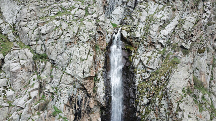 High waterfall among the rocks. View from a drone. Large rocks and steep slopes surround the...