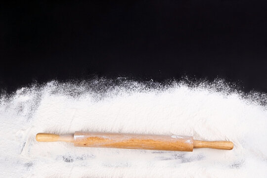 Rolling pin and white flour on a dark background. Free space for text .