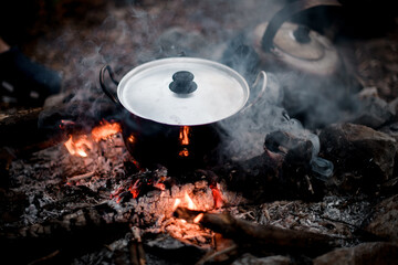 view of steaming iron pot with lid standing on the wood in fire.