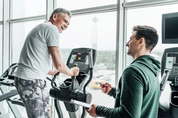 Foto op Canvas Portrait of an older man during training, his physiotherapist is standing next to him and tells how to do the exercise correctly © Тарас Нагирняк