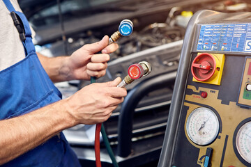 Mechanic holds a set of high-pressure pipes for filling the car's air conditioning system. A/C Manifold Gauges Set.