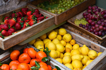 Fresh fruits in wooden boxes, blue and green grapes, lemons, strawberries, tangerines, advertising for organic farming and healthy food