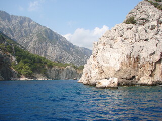 A natural picture of impregnable coastal rocks under the rays of the tropical sun reflected in the azure mirror of the sea bay.