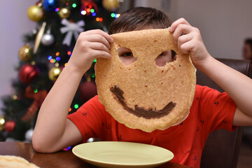 Little boy eating pancakes and make a smiley face from it. Child enjoy eating pancake and playing