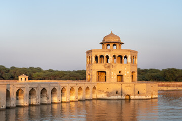 Fototapeta premium Sunset view of ancient octagonal pavilion and causeway bridge on water tank pool at mughal era Hiran Minar complex in Sheikhupura, Punjab, Pakistan