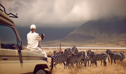 Woman traveler on safari-tour in Africa, traveling by car in Tanzania, watching wild animals and birds in the National park Ngorongoro - obrazy, fototapety, plakaty