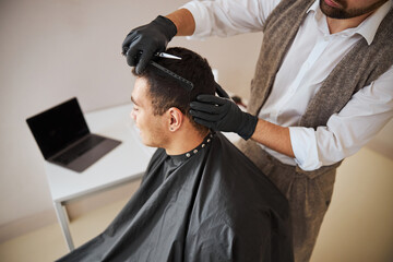 Professional hair stylist in gloves making hair styling in room indoors