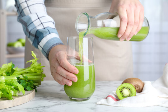 Woman Pouring Fresh Celery Juice Into Glass At White Marble Table, Closeup