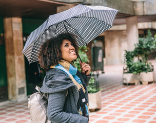 Afro American woman in coat and umbrella smiles while looking up