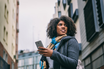 Fototapeta premium Attractive brunette girl with afro hair smiles while looking at mobile phone