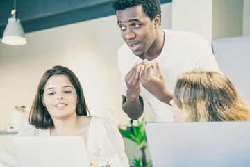 Obraz premium Designers team meeting and arguing about project. Diverse colleagues standing and sitting at table with laptops, looking and pointing at screen, talking and gesturing. Corporate meeting concept