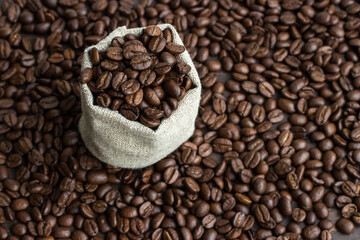 Roasted coffee beans in a canvas bag on a background of scattered beans