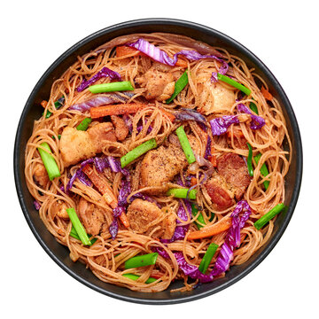 Pancit Bihon in black bowl isolated on white. Filipino cuisine noodles dish with pork belly, chicken, vegetables. Asian food. Top view