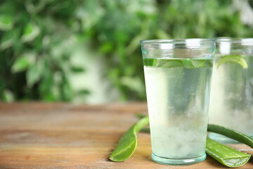 Fresh aloe drink in glasses and leaves on wooden table, space for text