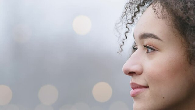 Side view portrait female profile african american woman with curly hair breathes cold air looks away to side waiting, close-up female beautiful face with perfect dark skin and afro hairstyle outdoors