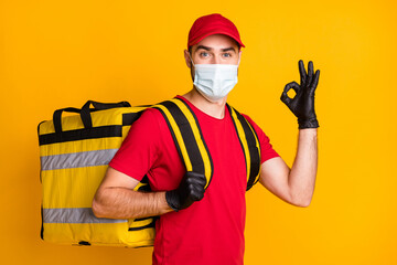 Portrait of nice content healthy guy mailman wear gauze mask carrying bag order showing ok-sign isolated on bright yellow color background