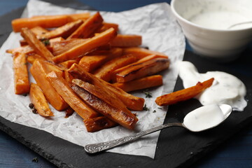 Slate plate with deliciously cooked sweet potatoes, rosemary, sauce and spices, herbs on a wooden table