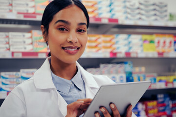 Happy young woman working in chemist in labcoat using digital tablet in pharmacy