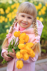 Portrait Cute little girl holding a bouquet of yellow tulips on the background of beautiful flowers.