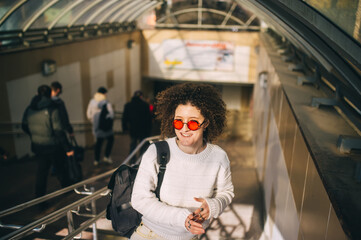 Curly woman with red glasseson the escalator in the city.