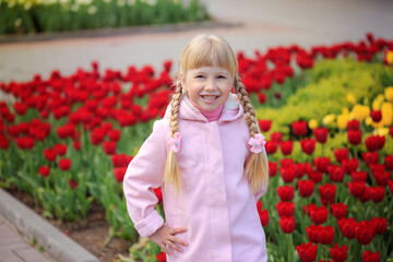 Sweet beautiful girl in a pink coat walks on a spring city. Sunny day. Red and yellow tulips