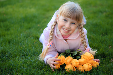 Portrait of a girl with bright yellow tulips. Bright sunny Easter day. Girl lies on a green lawn