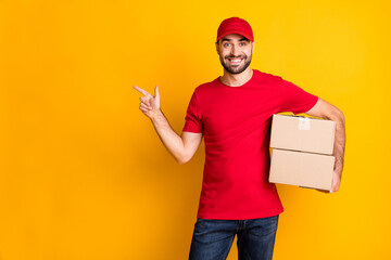 Photo of cute guy courier dressed red clothes delivering brown box pointing empty space isolated...