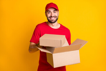 Photo of cheerful guy courier dressed red clothes holding delivering brown boxes isolated yellow color background