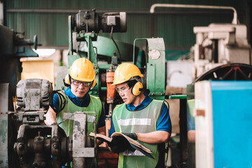 Work at factory.Two Asian workers man team working together in safety work wear with yellow helmet using Manual book.in factory workshop industry meeting professional