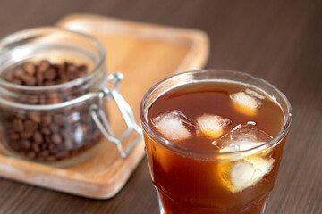 Ice coffee with ice cubes and jar with coffee beans on wooden plate. Cold brew.