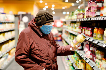 Old senior woman wear medical mask, protection against pandemic coronavirus disease. 90 years retired female lady push cart trolley for shopping in supermarket. Woman buy food and groceries