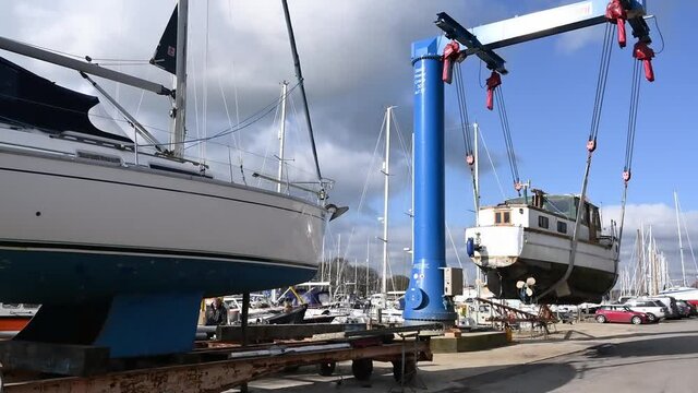 A boat lifted by a crane out of Birdham Pool Marina and sitting in the air in a boat Hoist awaiting a low trailer.